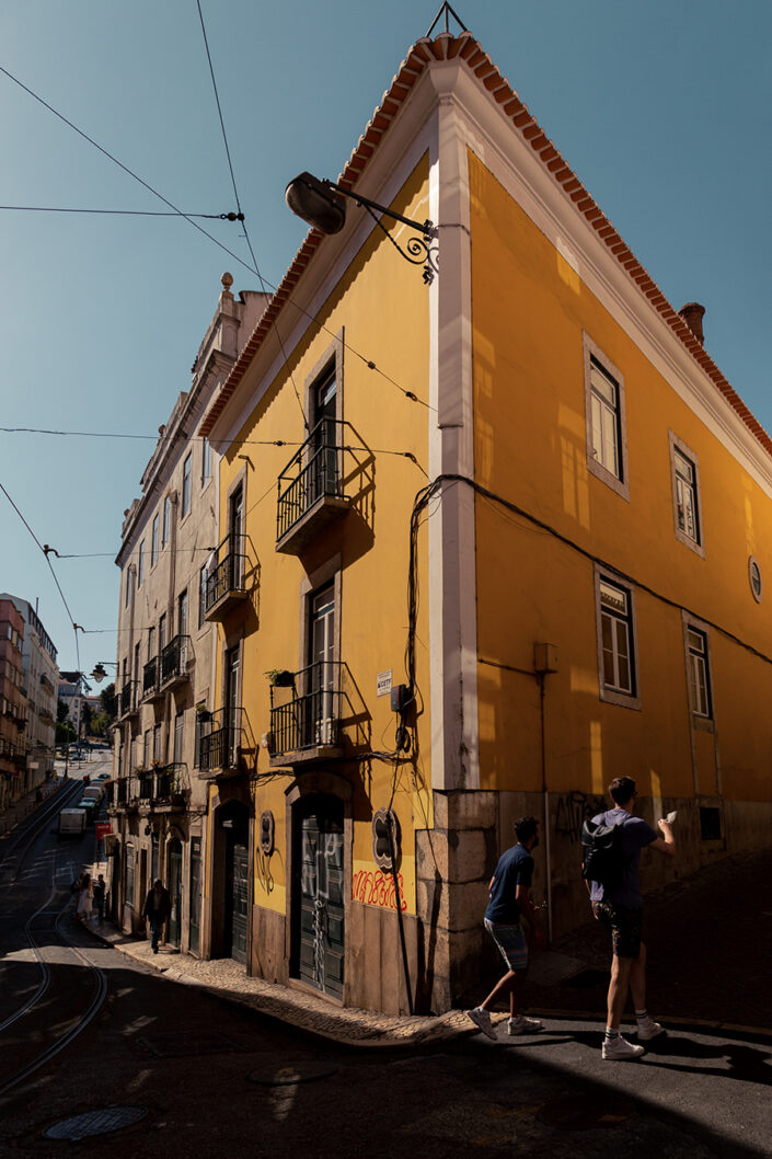 Ein gelbes Eckhaus und Fußgänger in Lissabon