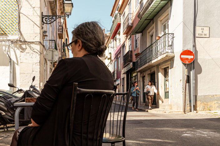 Eine Frau sitzt am Straßenrand in Lissabon an einem Tisch und trinkt Kaffee