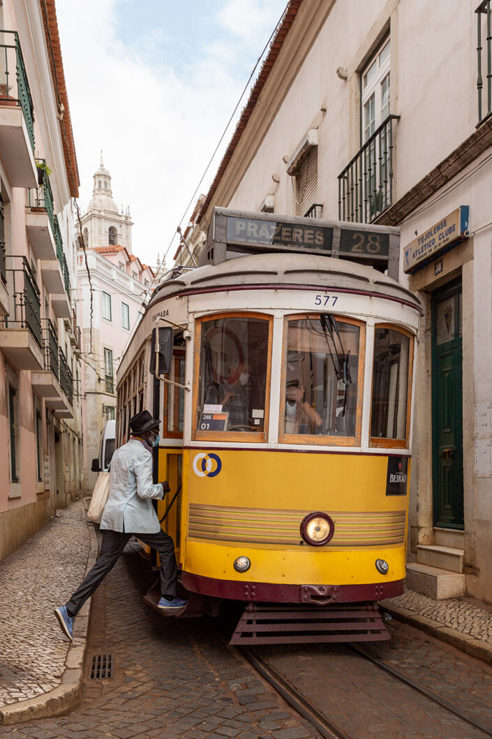 Ein elegant gekleideter Mann steigt in die berühmte Tram 28, in einer engen Lissabonner Gasse