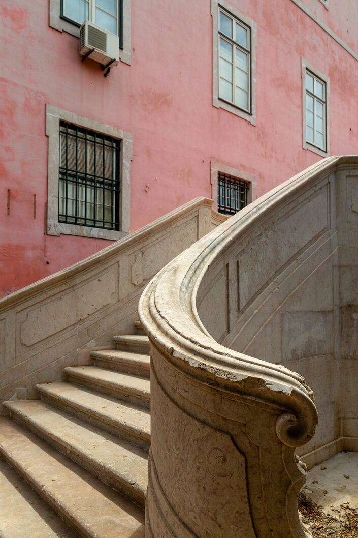 Eine geschwungene Steintreppe vor einer rosaroten Mauer