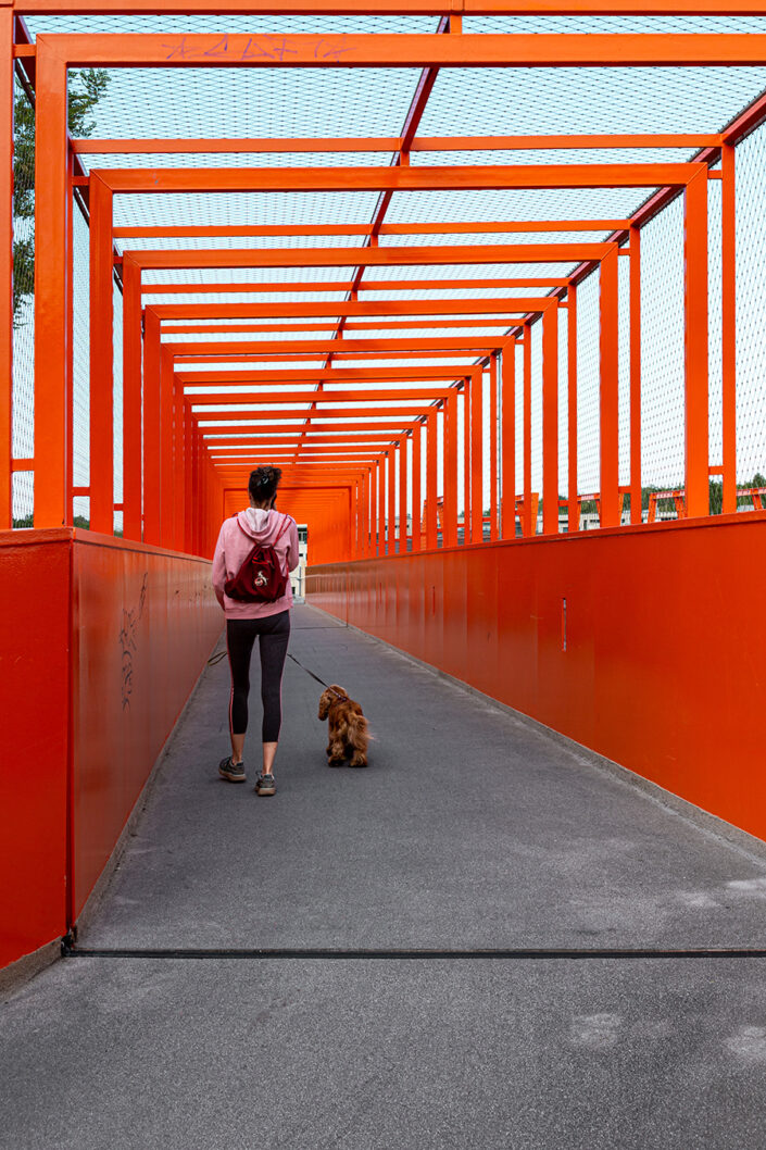 Eine junge Frau mit Hund geht über die auffällige orange Belvederebrücke